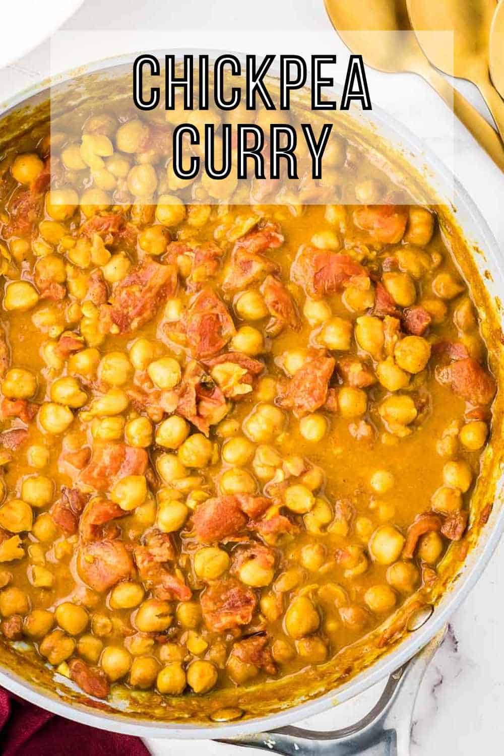 Overhead shot of chickpea curry in a skillet on a marble countertop with golden spoons on the side.