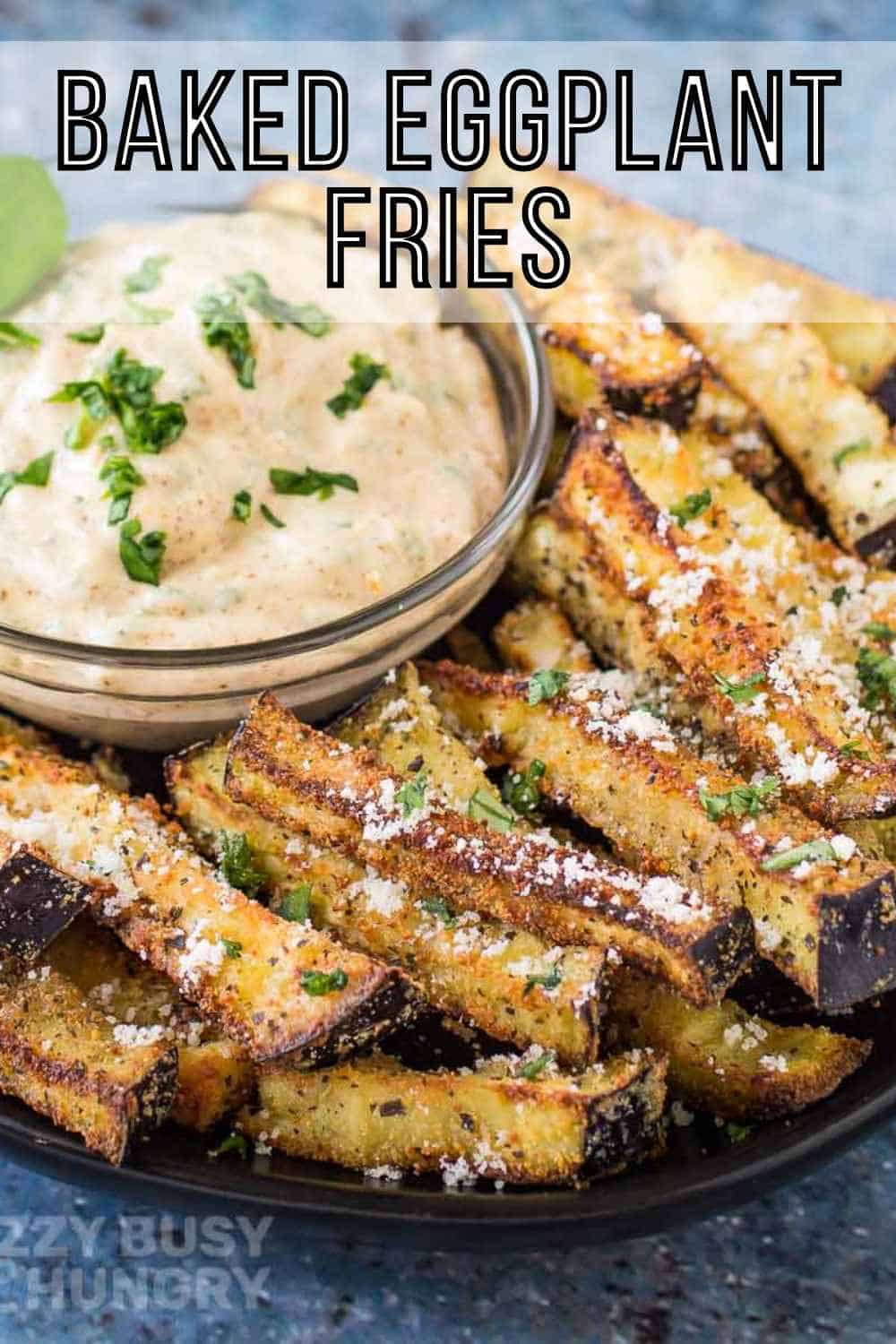 Side angled shot of eggplant fries garnished with basil and parmesan on a black plate with a clear bowl of chipotle basil dip garnished with more fresh basil.
