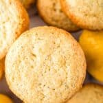 Overhead shot of lemon muffins stacked on a white surface with whole lemons in the background.