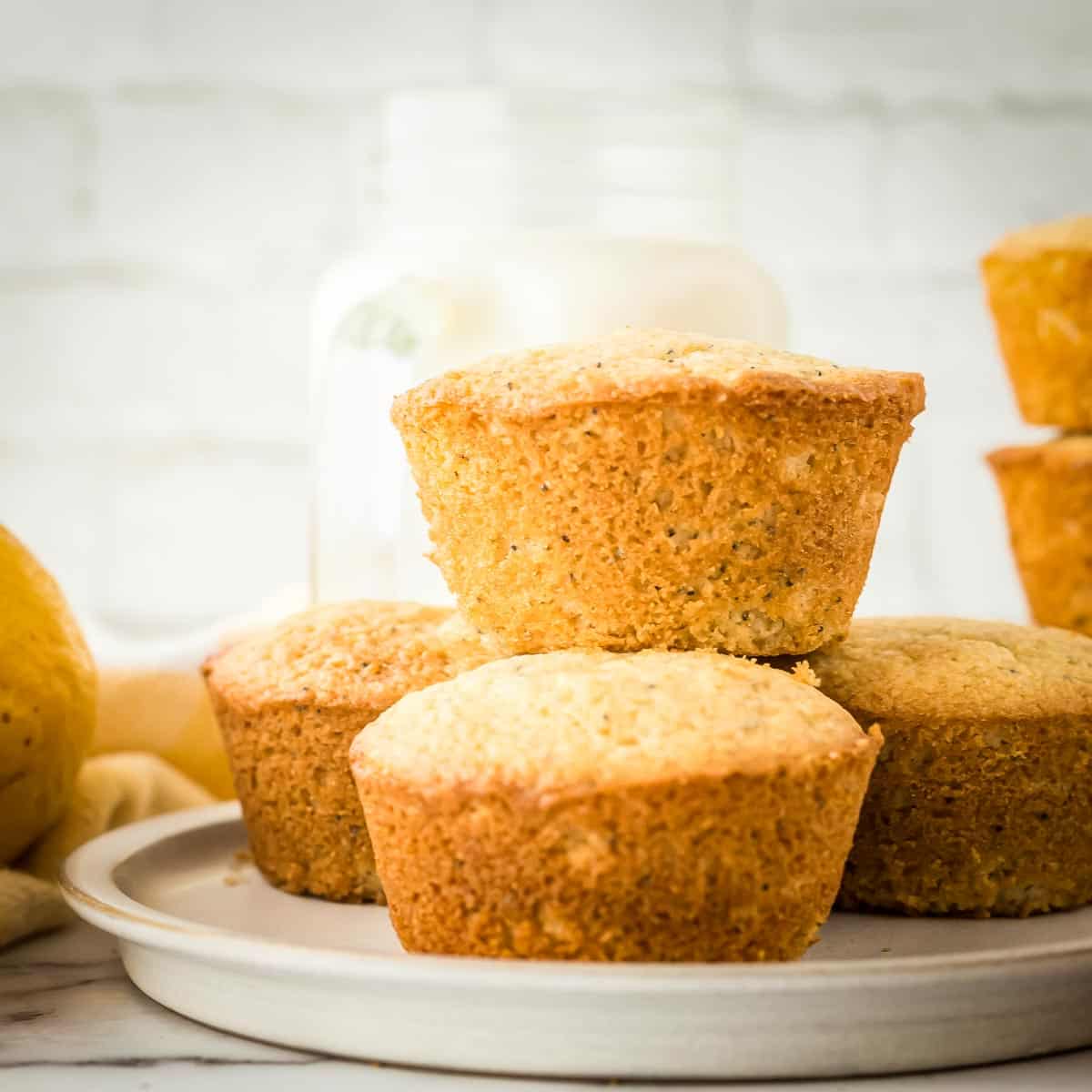 Side shot of lemon muffins stacked on a grey plate with whole lemons in the background.