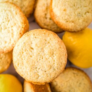 Overhead shot of lemon muffins stacked on a white surface with whole lemons in the background.
