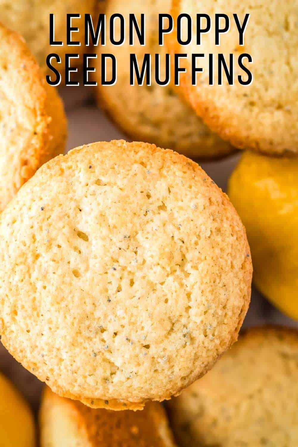 Overhead shot of lemon muffins stacked on a white surface with whole lemons in the background.