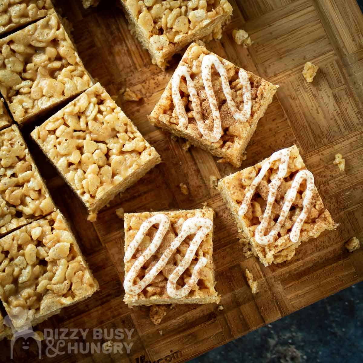 Overhead shot of Rice Krispie treats with icing drizzle on a wooden cutting board.