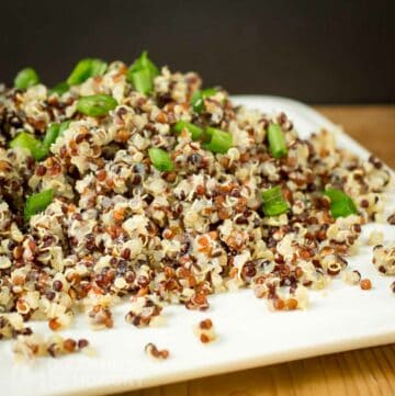Side shot of quinoa garnished with green onions on a square white plate on a wood table.