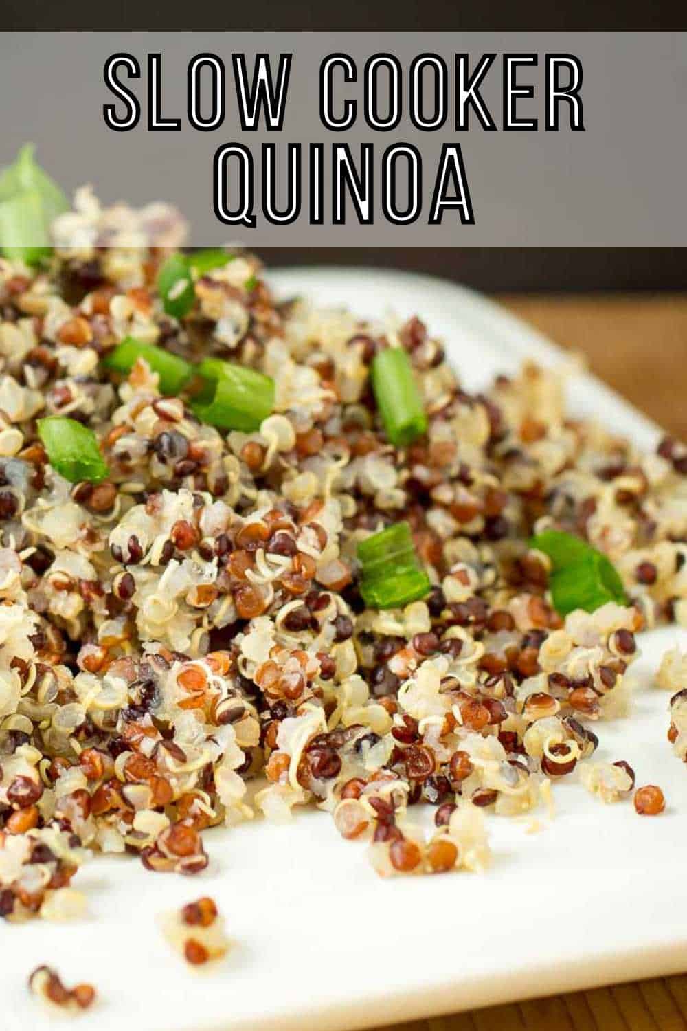 Close up side shot of quinoa garnished with green onions on a square white plate on a wood table.