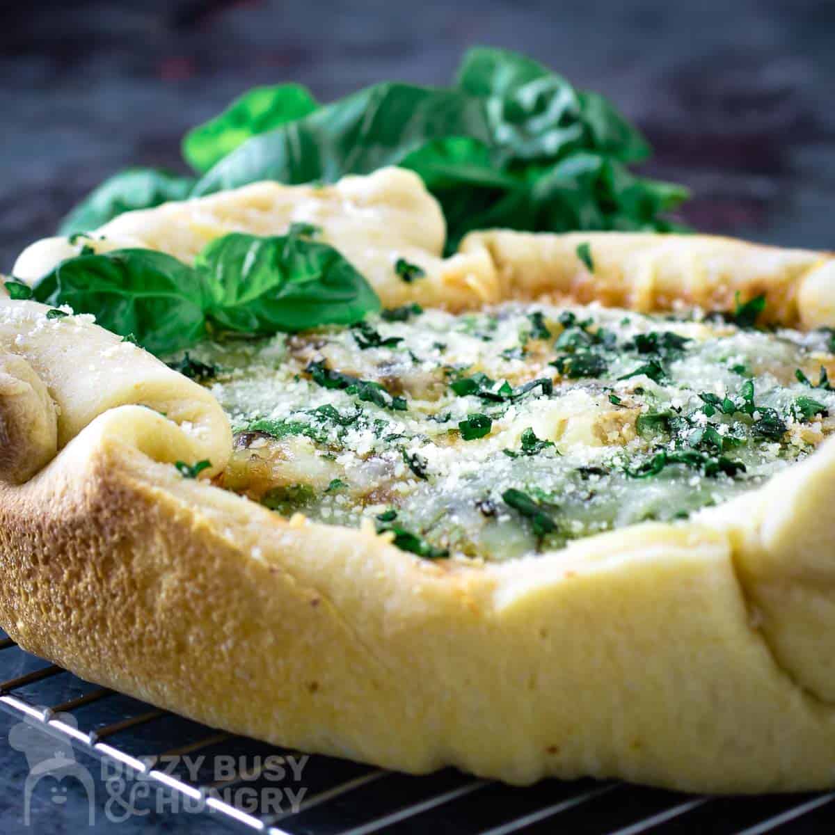 Side close up shot of crock pot pizza garnished with basil on a wire cooling rack.