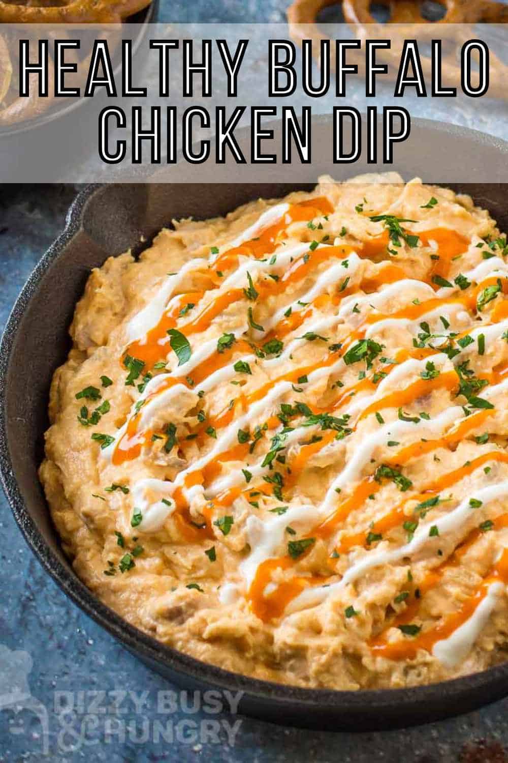 Side angled shot of buffalo chicken dip garnished with buffalo sauce, sour cream, and herbs in a cast iron skillet with a bowl of pretzels in the background.