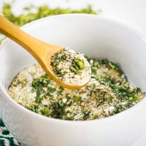 Side close up shot of a wooden spoon scooping some ranch seasoning out of a white bowl.