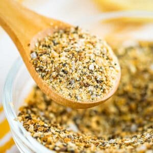 Side close up shot of a wooden spoon scooping some seasoning from a clear bowl full of seasoning.