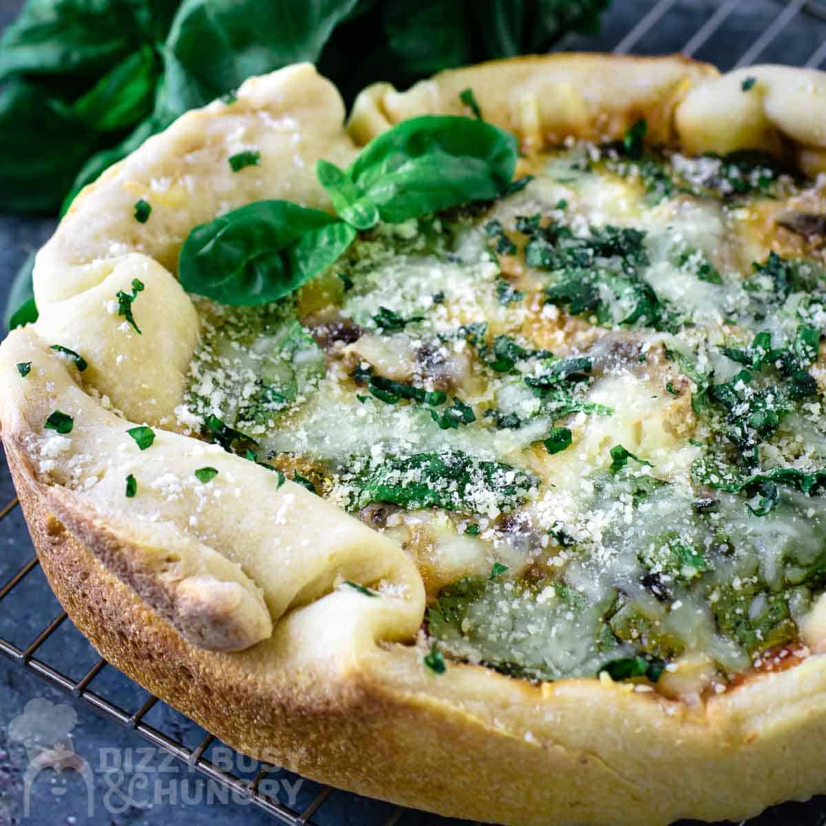 Side close up shot of crock pot pizza garnished with basil on a wire cooling rack.