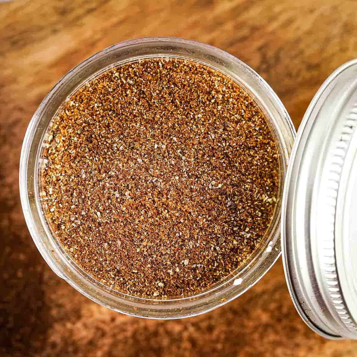 Overhead shot of clear mason jar full of chili seasoning with the metal lid leaning on the side on a wooden table.