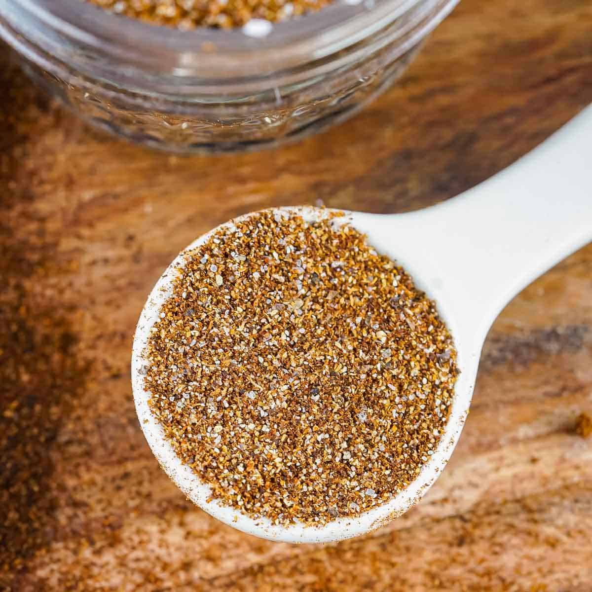 Close up shot of a white ceramic spoon full of chili seasoning on a wooden table.