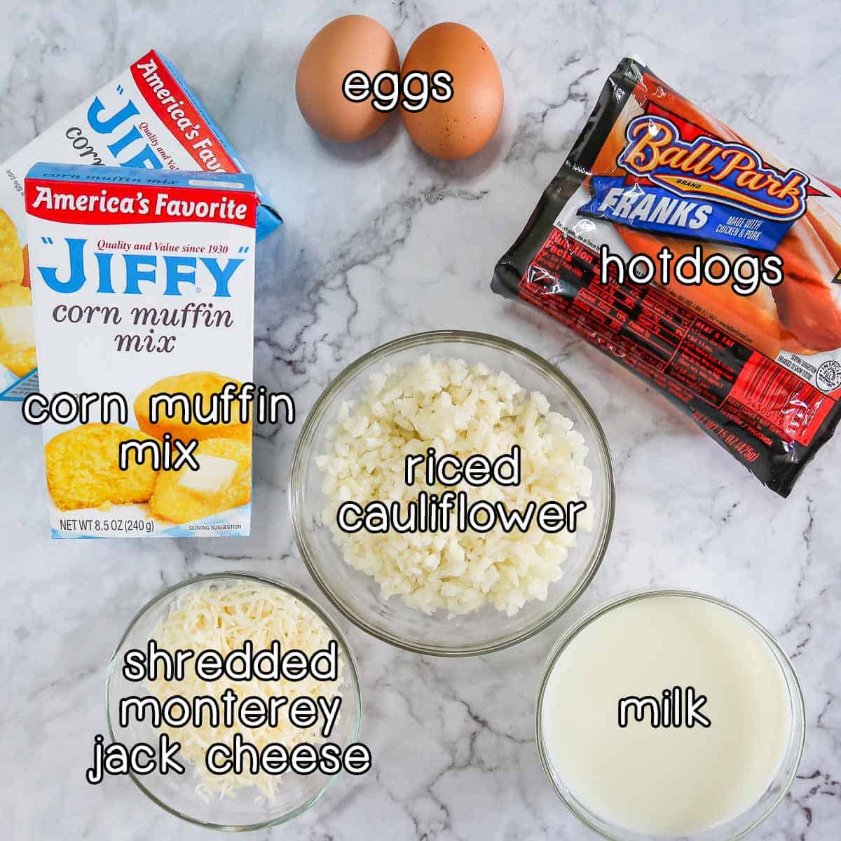 Overhead shot of ingredients - corn muffin mix, eggs, hotdogs, riced cauliflower, shredded Monterey Jack cheese, and milk.