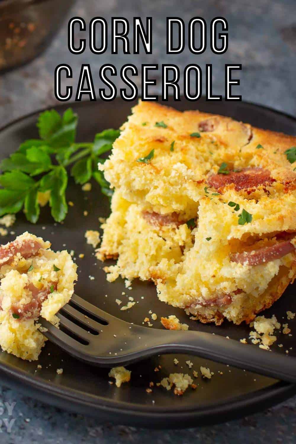 Side shot of a slice of casserole garnished with herbs on a black plate with a black fork holding a piece of casserole on the side.