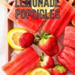 Overhead shot of popsicles on a bed of ice in a pink bowl with lemon slices and strawberries.