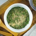 Overhead shot of seasoning in a white bowl on a wooden surface with wooden spoons on the side.