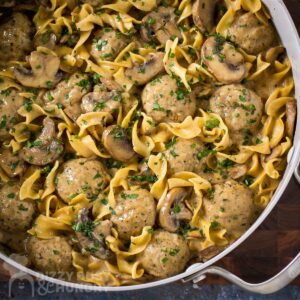Overhead shot of a large silver pot full of meatball stroganoff on a wooden surface.