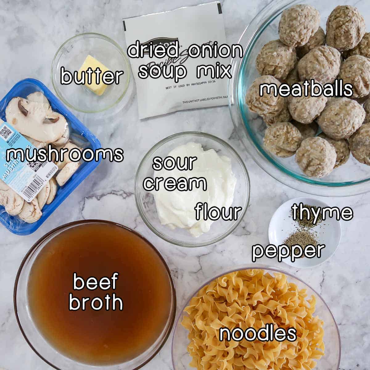 Overhead shot of ingredients - butter, dried onion soup mix, meatballs, mushrooms, sour cream, flour, thyme, pepper, noodles, and beef broth.