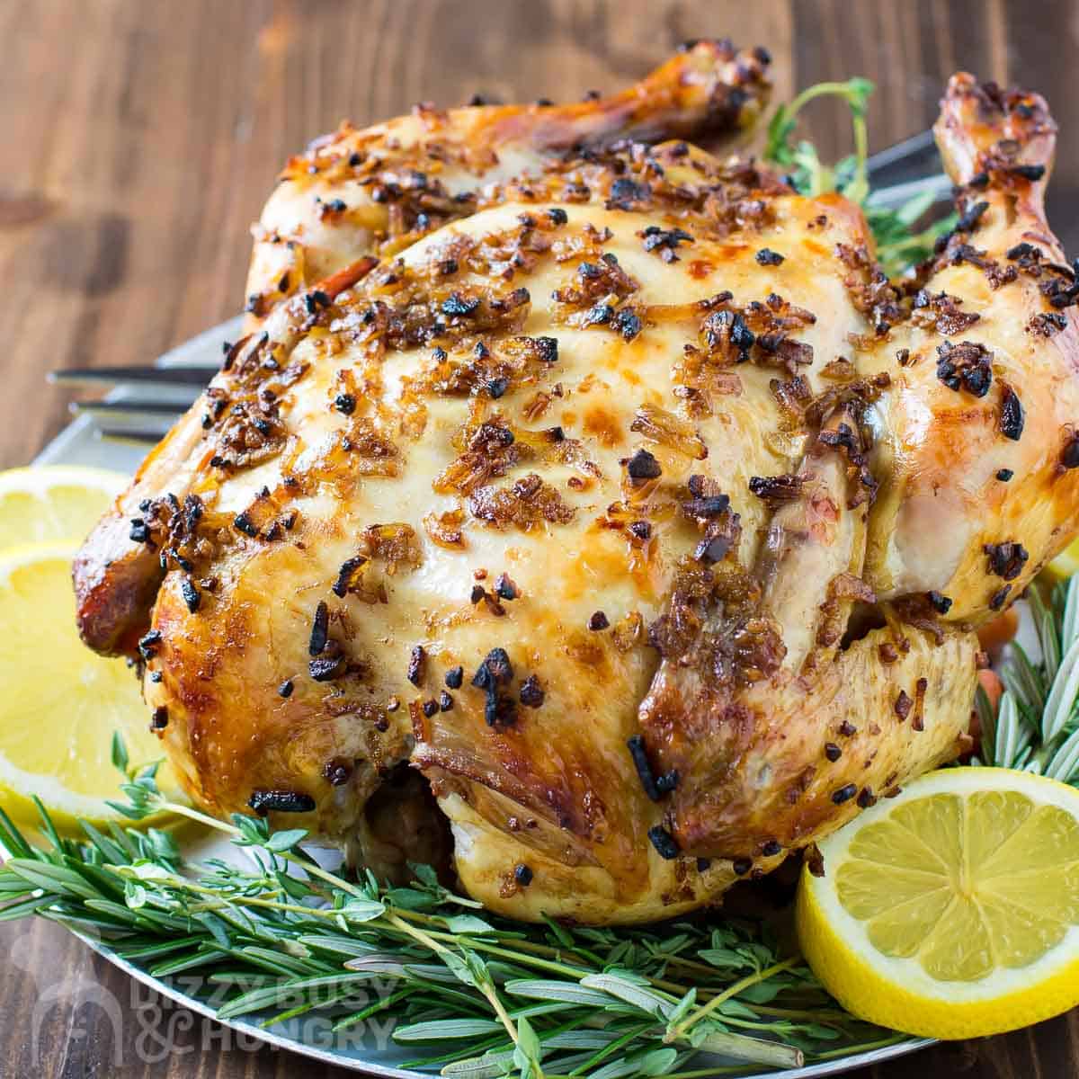 Side shot of whole crock pot chicken on a bed of thyme and sliced lemons on a blue plate with a fork on the side.