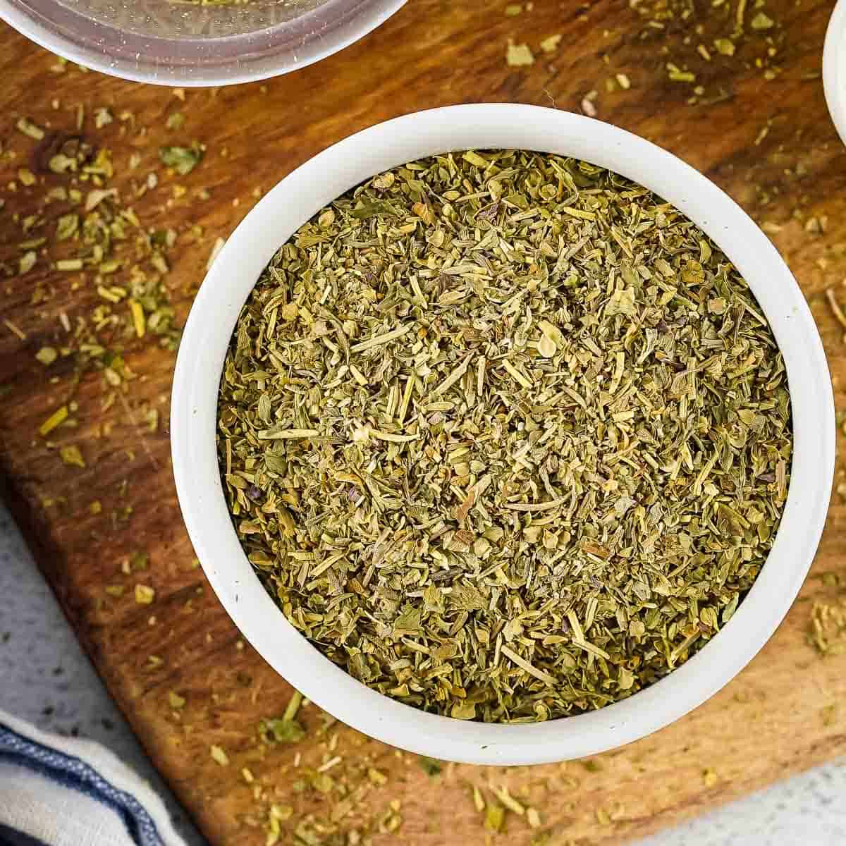 Overhead shot of seasoning in a white bowl on a wooden surface with more seasoning scattered around.