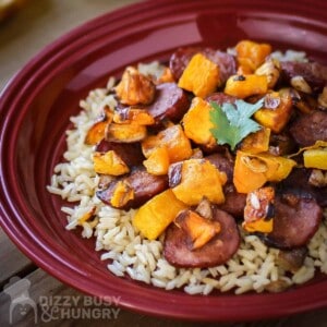 Side close up shot of sausage and butternut squash on a bed of rice on a red plate.