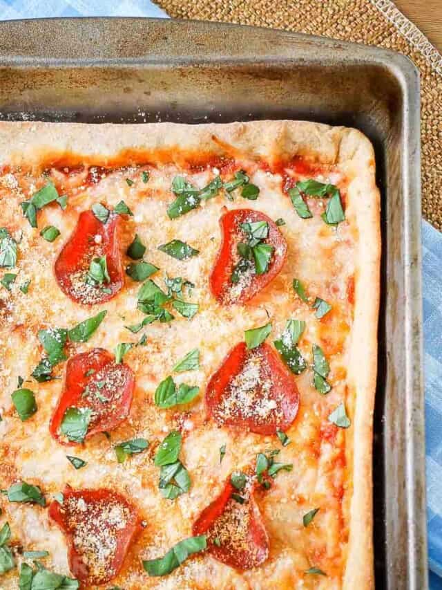 Overhead close up of full pan pizza garnished with parmesan cheese and basil on a blue plaid cloth.