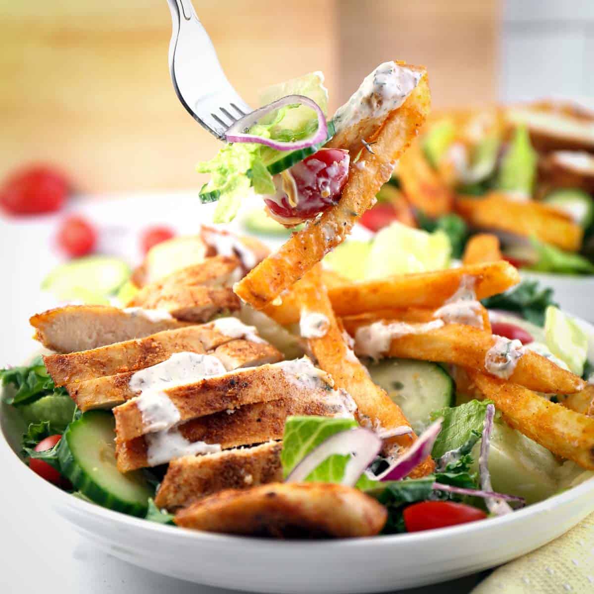 Side shot of a fork picking up a bite of Pittsburgh salad drizzled with ranch in a white plate on a pale yellow cloth.
