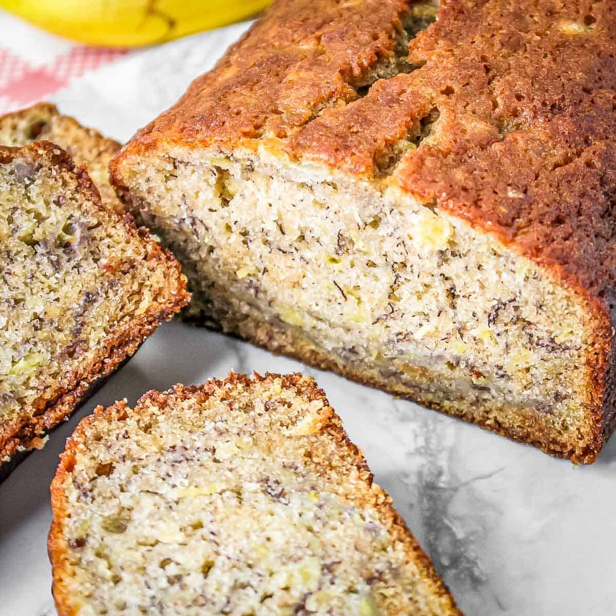 Side shot of whole pineapple banana bread with a few slices on a marble surface.