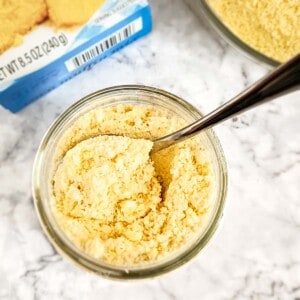 Overhead shot of a small clear bowl with cornbread mix and a spoon on a marble surface and a cornbread mix box in the background.