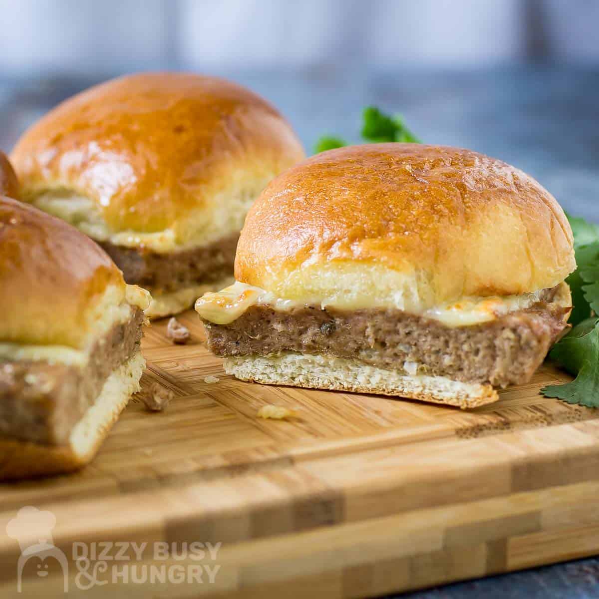 Side shot of three turkey burger sliders on a wooden cutting board with herbs on the side.