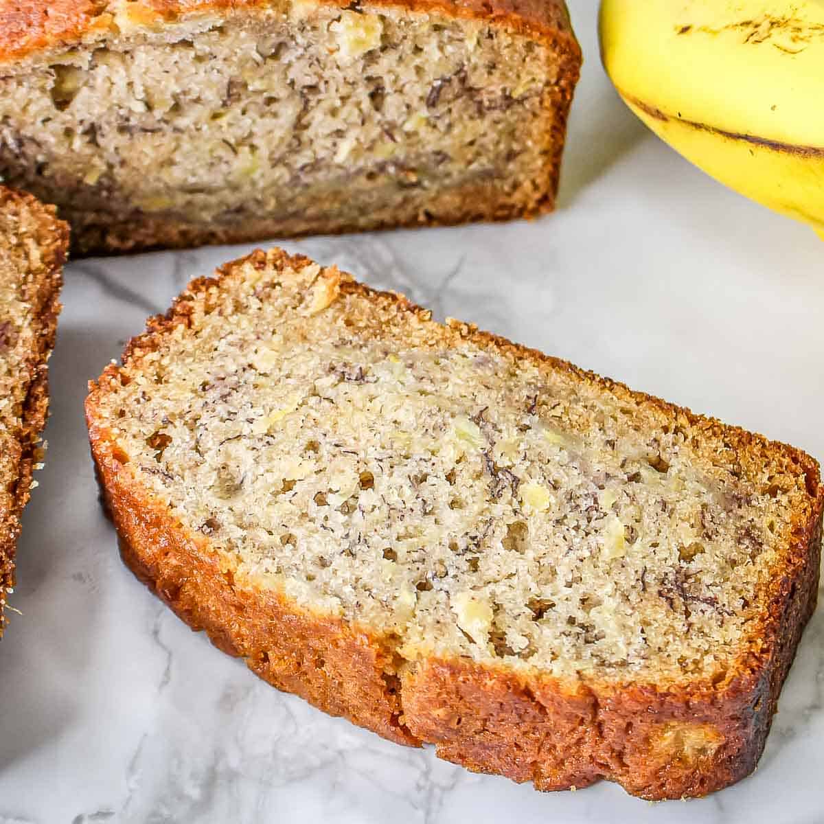 Side close up shot of pineapple banana bread on a marble surface with a banana on the side.