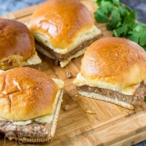 Side angled shot of three turkey burger sliders on a wooden cutting board with herbs on the side.