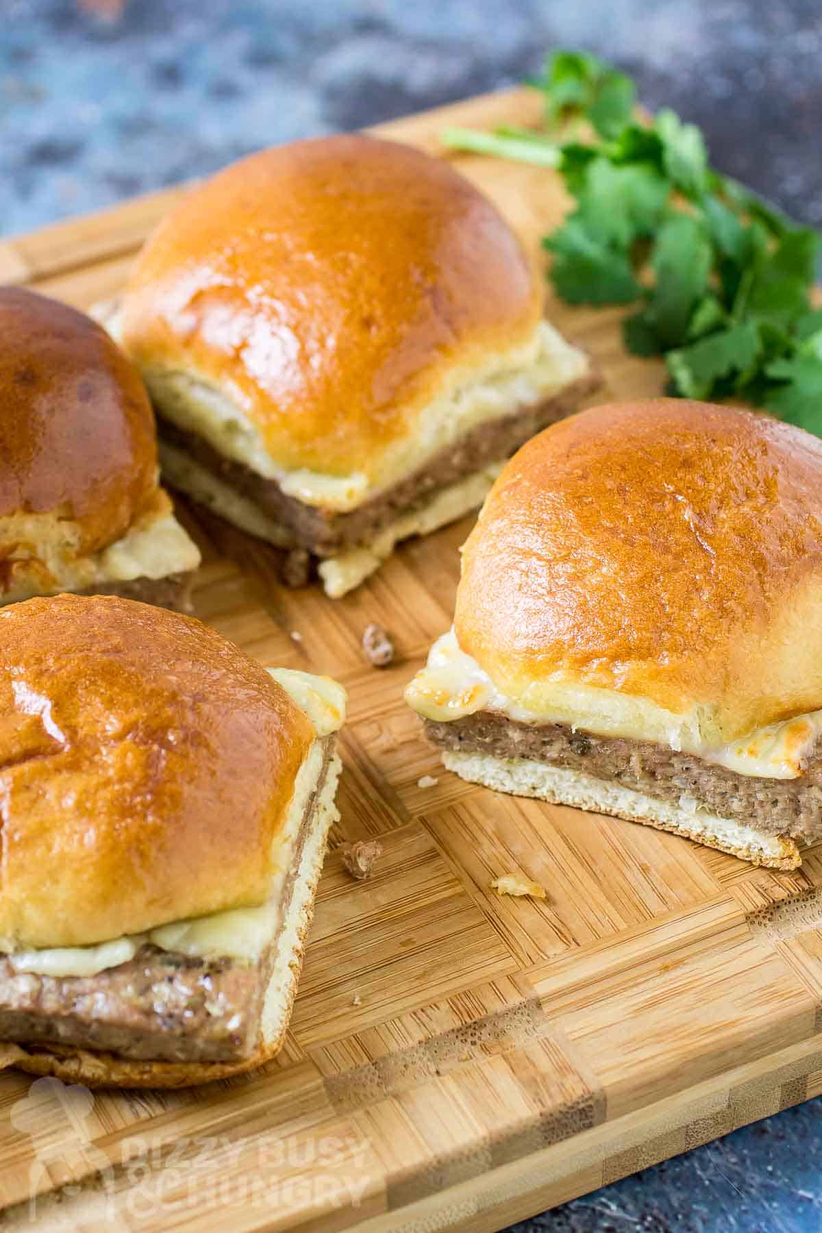 Side angled shot of three turkey burger sliders on a wooden cutting board with herbs on the side.