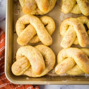 Overhead shot of soft pretzels arranged on a baking sheet with an orange towel on the side.