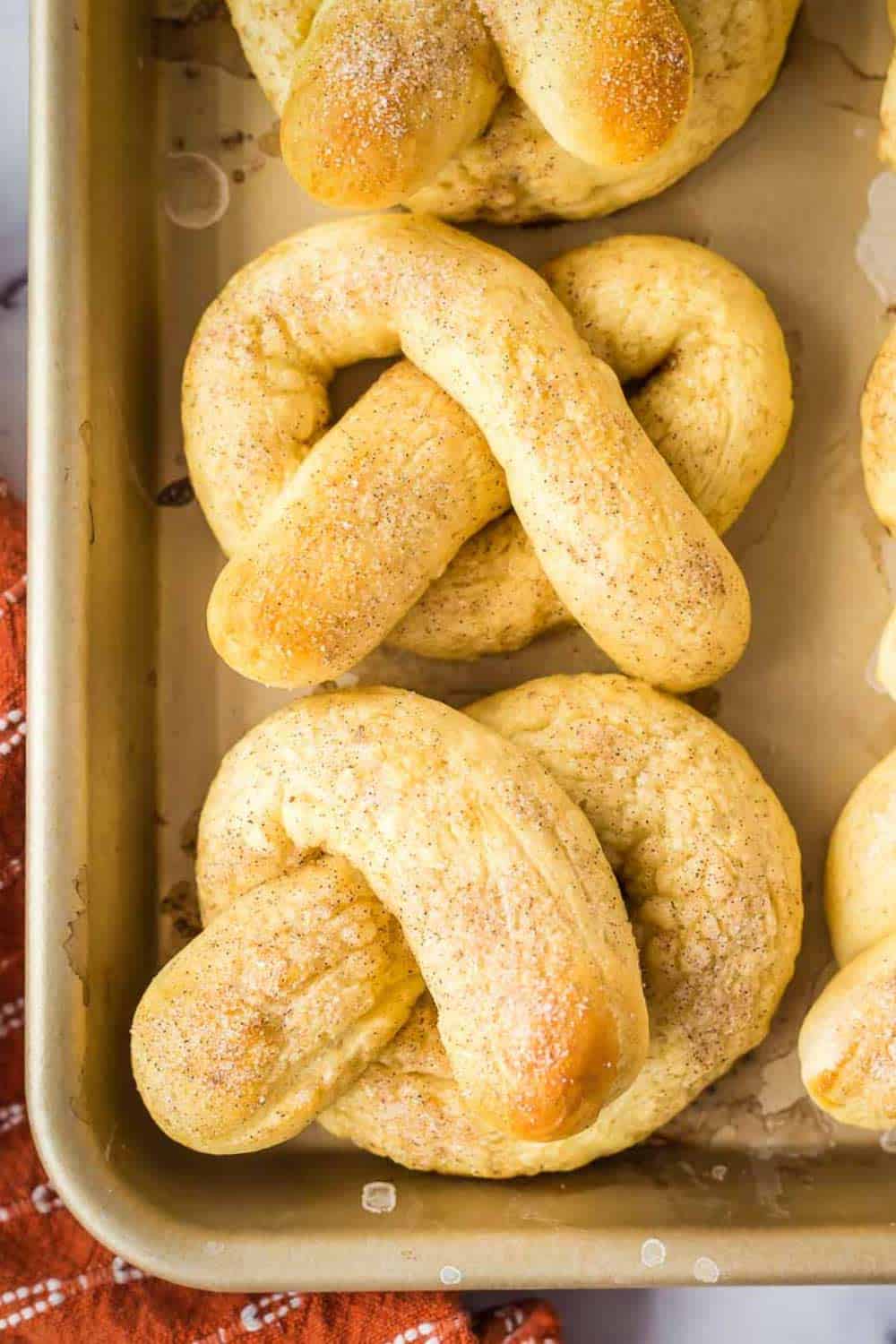 Overhead shot of soft pretzels arranged on a baking sheet with an orange towel on the side.