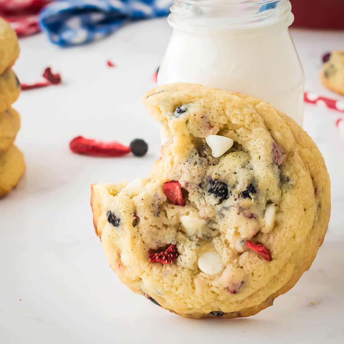 Side close up shot of a cookie with a bite taken out leaning on a glass jar with freeze dried fruits in the background.