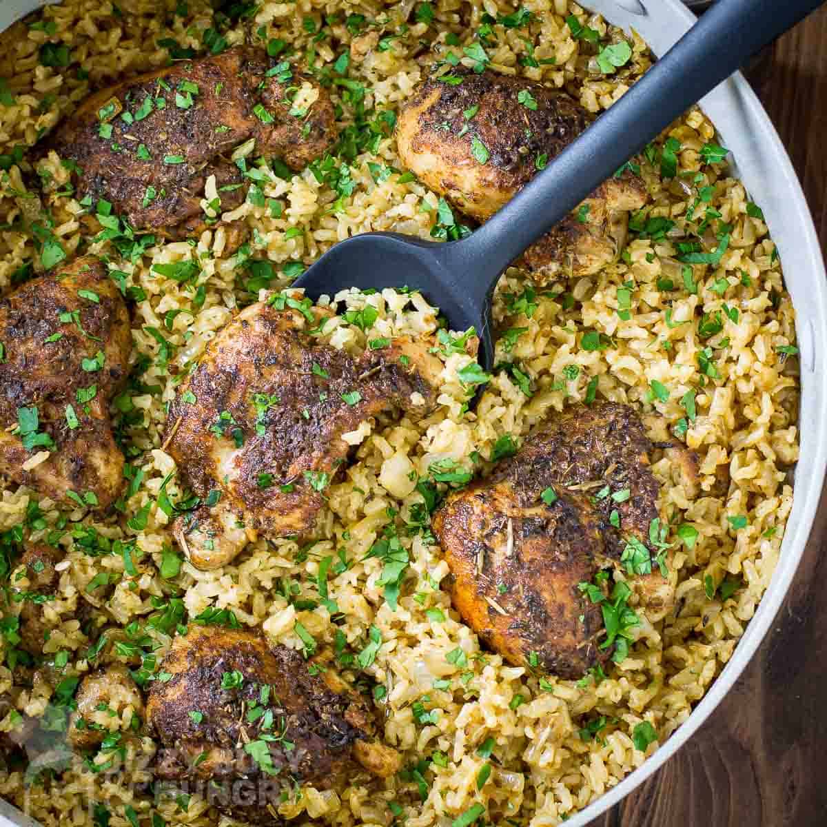 Overhead shot of chicken and rice garnished with herbs being scooped out of a large white bowl.