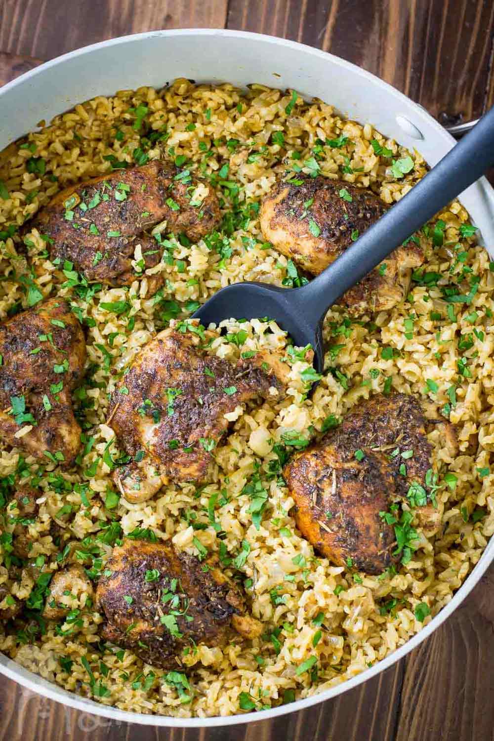 Overhead shot of chicken and rice garnished with herbs being scooped out of a large white bowl on a wooden surface.