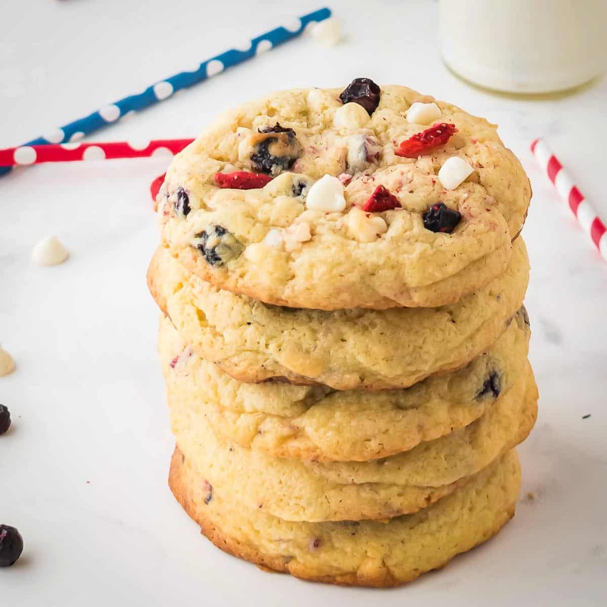 Side angled shot of multiple cookies stacked on each other on a white surface with red white and blue straws in the background.