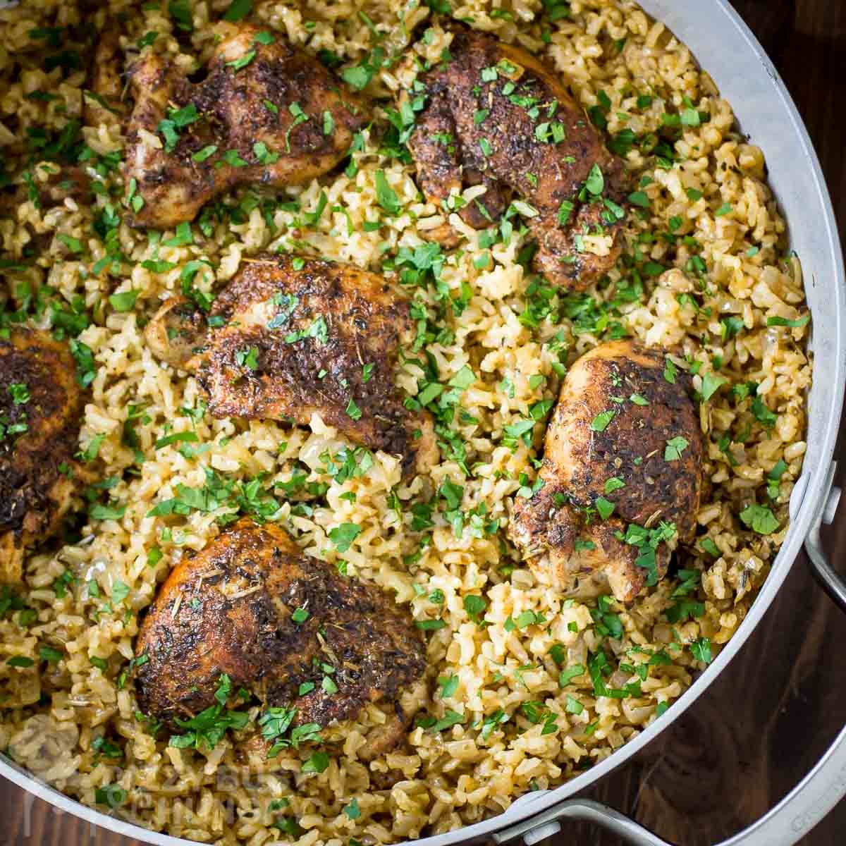 Overhead shot of chicken and rice garnished with herbs in a large pot on a wooden surface.