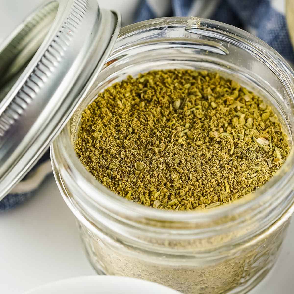 Side angled shot of poultry seasoning in a clear mason jar with the lid leaning on the side.