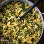 Overhead shot of spinach and mushroom pasta in a large pot with a rubber spoon on a wooden table.