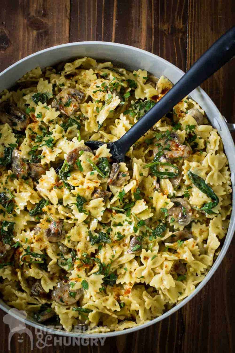 Overhead shot of spinach and mushroom pasta in a large pot with a rubber spoon on a wooden table.