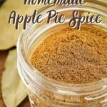 Side angled shot of pumpkin pie spice in a small clear mason jar on a wooden cutting board with bay leaves in the background.
