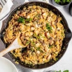 Close up overhead shot of orzo pasta garnished with fresh herbs in a large skillet with a Woden spoon and white cloth on the side.
