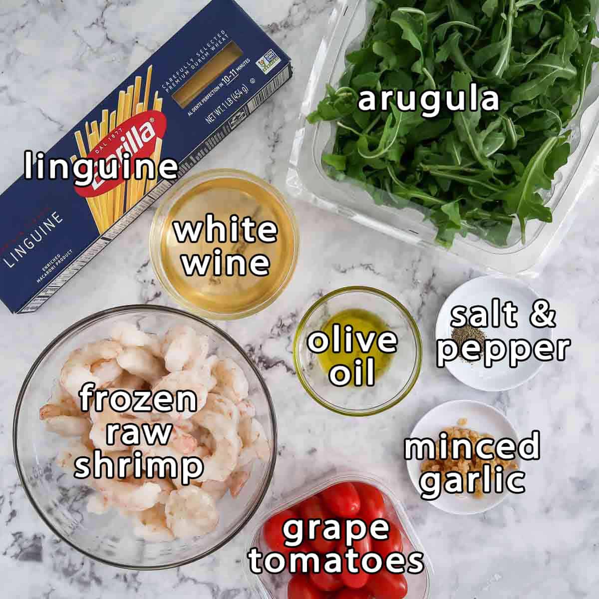 Overhead shot of ingredients - linguine, arugula, white wine, olive oil, frozen raw shrimp, grape tomatoes, minced garlic, salt, and pepper.