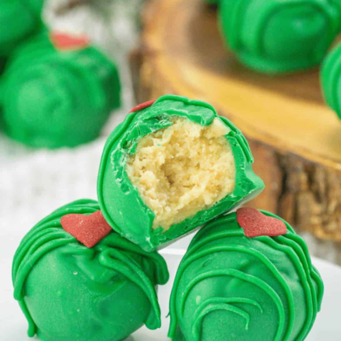 Golden one inch dough balls covered in Grinch green candy melt and decorated with small red hearts.