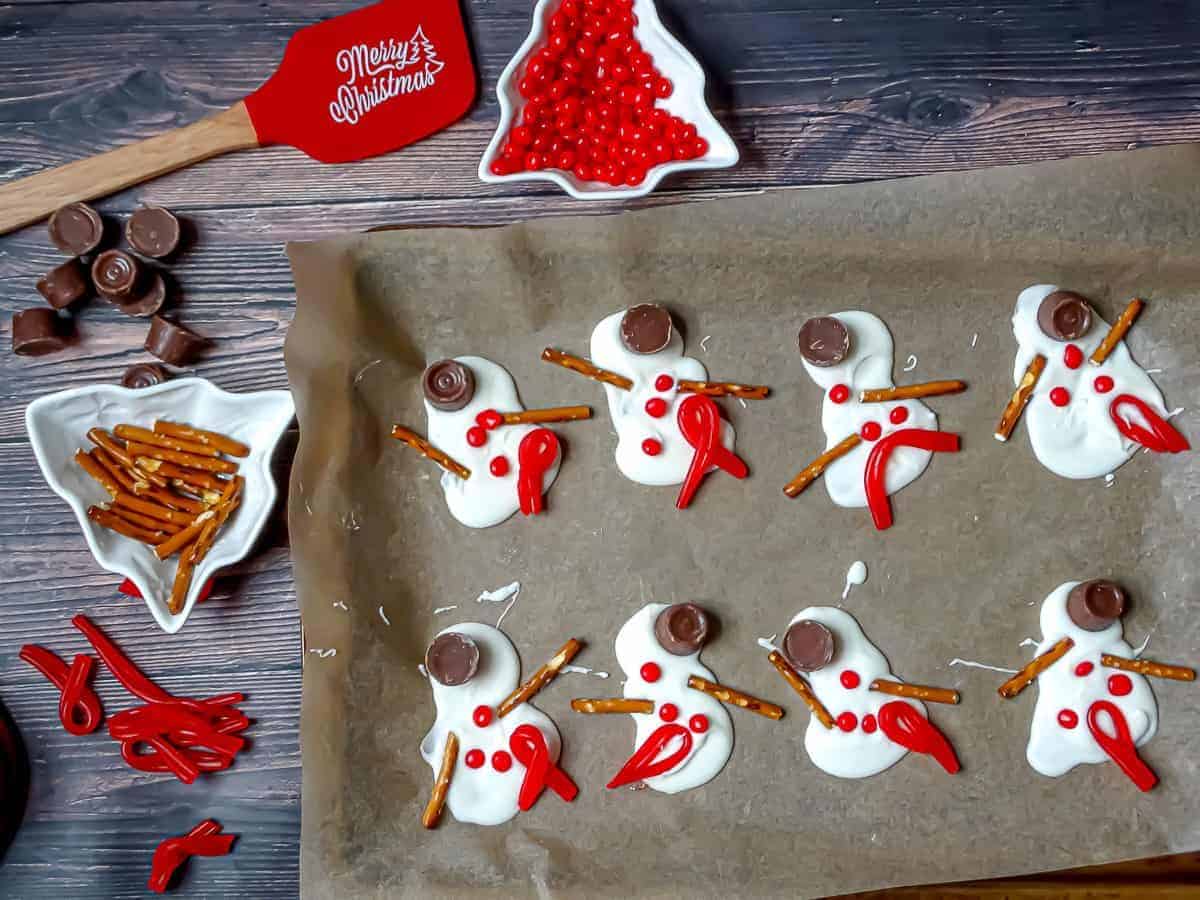 White chocolate blobs on a cookie tray that are decorated with pretzels and candy to look a snowman that has melted.