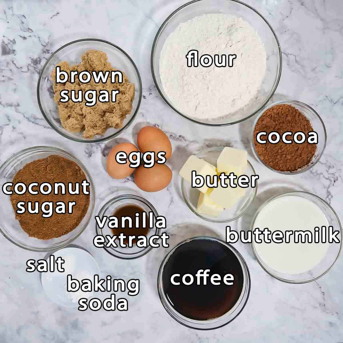 Overhead shot of cake ingredients - flour, brown sugar, coconut sugar, cocoa, eggs, vanilla extract, butter, buttermilk, coffee, salt, and baking soda.