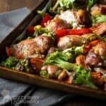 Side close up shot of chicken thighs and veggies on a baking sheet.